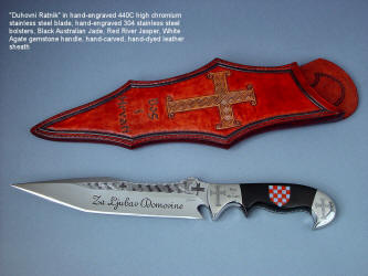 "Duhovni Ratnik" obverse side view. Knife in hand-engraved 440C high chromium stainless steel blade, hand-engraved 304 stainless steel bolsters, handle of Black Nephrite Jade gemstone inlaid with a mosaic of Red River Jasper and White Geodic Quartz. Sheath is hand-carved, hand-dyed leather shoulder